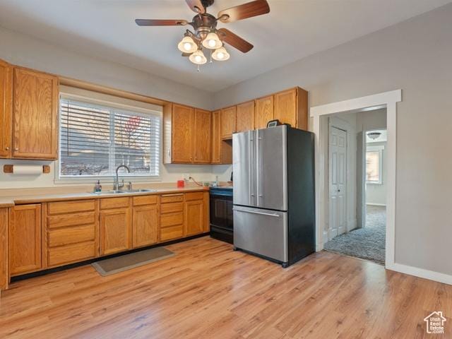 kitchen with freestanding refrigerator, a sink, stove, and light wood finished floors