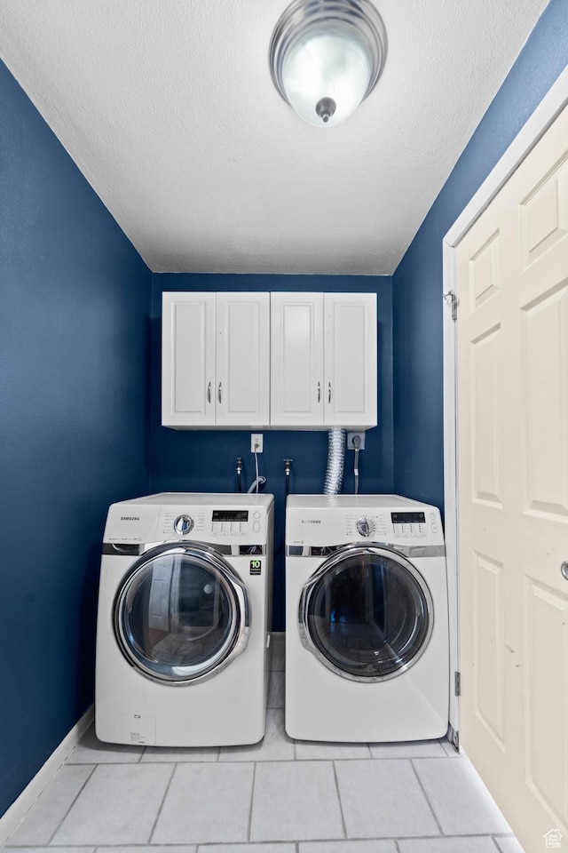 laundry room with a textured ceiling, baseboards, washing machine and dryer, cabinet space, and light tile patterned floors