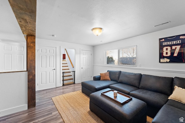 living room with stairs, wood finished floors, a textured ceiling, baseboards, and visible vents