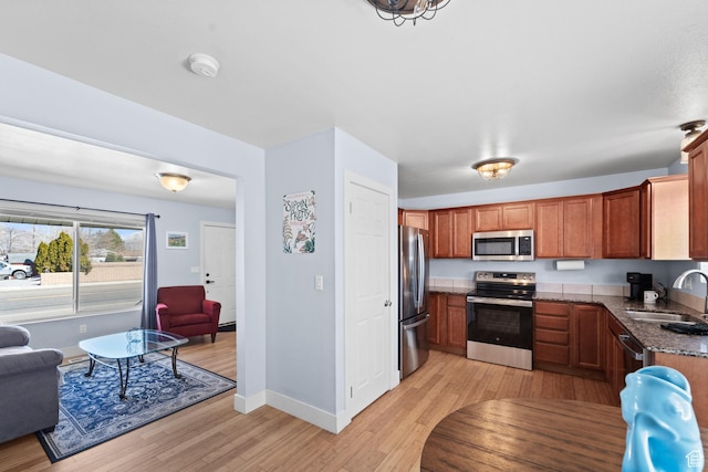 kitchen featuring baseboards, stainless steel appliances, a sink, light wood-type flooring, and brown cabinetry