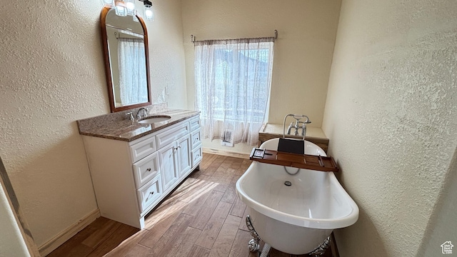 full bath with a textured wall, wood finished floors, vanity, baseboards, and a freestanding tub