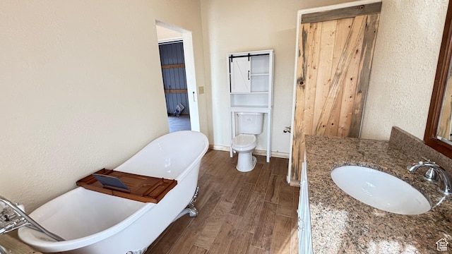 bathroom with wood finished floors, toilet, vanity, and a textured wall