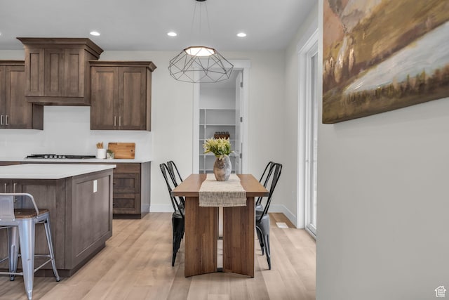 6579 W Bonnie Jean Ln Unit 12, Herriman, UT 84096 - kitchen with light countertops, a kitchen bar, decorative light fixtures, light wood-type flooring, and dark brown cabinetry