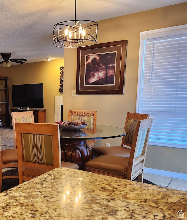dining space featuring ceiling fan with notable chandelier, tile patterned flooring, baseboards, and a textured ceiling