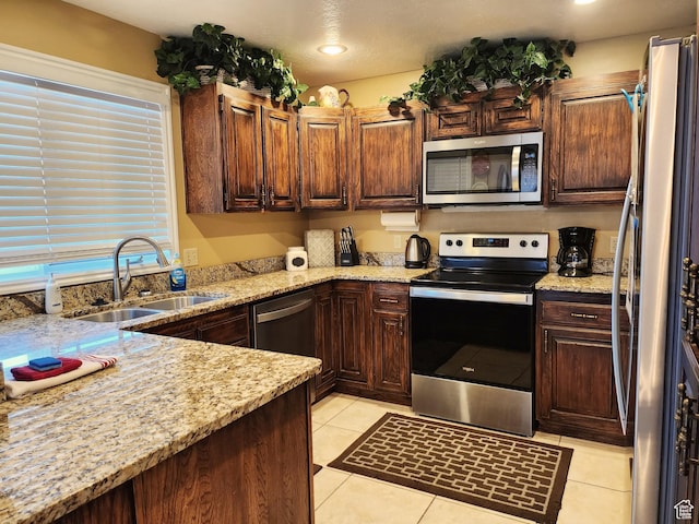 kitchen with a sink, light stone countertops, appliances with stainless steel finishes, light tile patterned floors, and recessed lighting