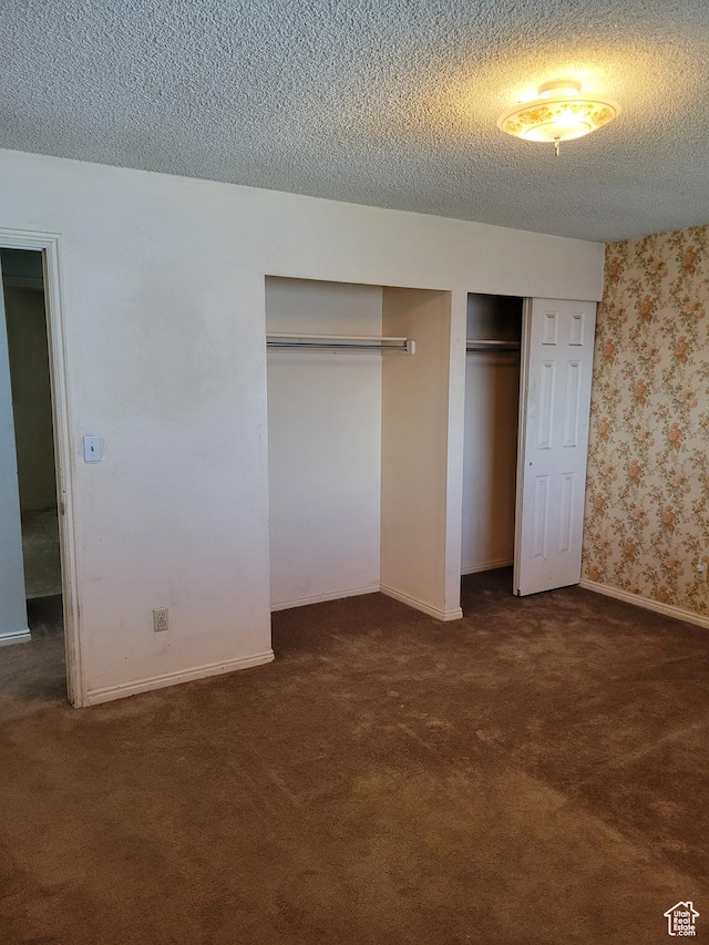 unfurnished bedroom with carpet, a textured ceiling, multiple closets, wallpapered walls, and baseboards