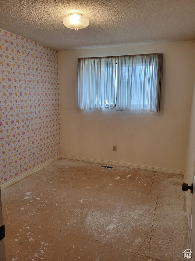empty room featuring a textured ceiling, wallpapered walls, and a healthy amount of sunlight