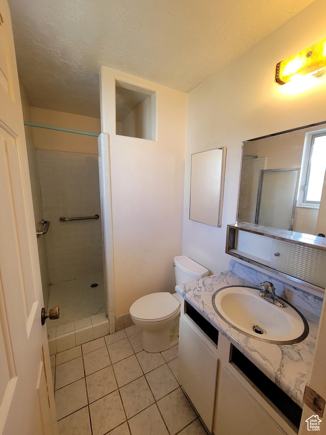 full bath featuring a textured ceiling, tiled shower, vanity, tile patterned flooring, and toilet