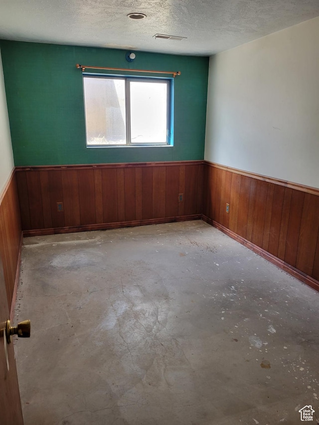 empty room featuring a textured ceiling, concrete floors, wainscoting, and visible vents