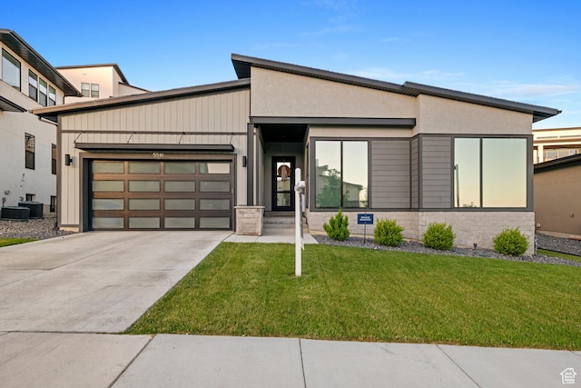 contemporary house featuring concrete driveway, stucco siding, an attached garage, stone siding, and a front yard