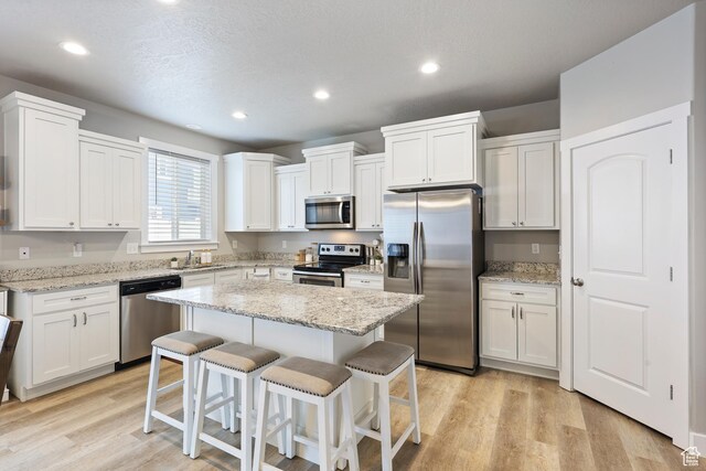 kitchen with white cabinetry, light wood-type flooring, a kitchen bar, and appliances with stainless steel finishes