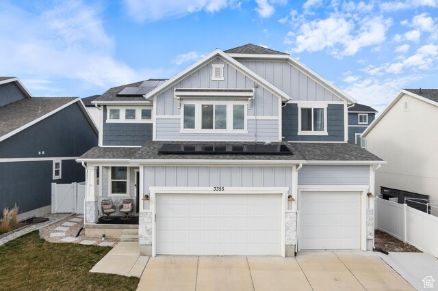 view of front of house featuring stone siding, board and batten siding, concrete driveway, and fence