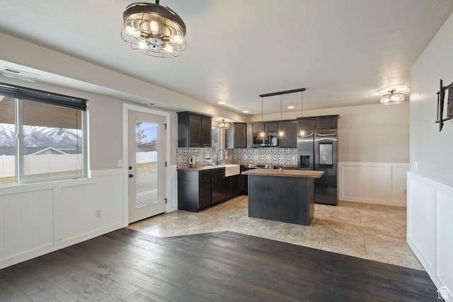 kitchen featuring appliances with stainless steel finishes, a center island, a chandelier, wainscoting, and light wood-style flooring