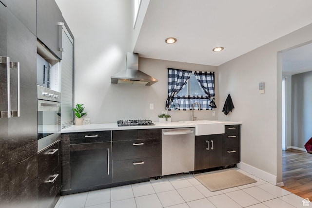 kitchen with a sink, wall chimney exhaust hood, appliances with stainless steel finishes, baseboards, and recessed lighting