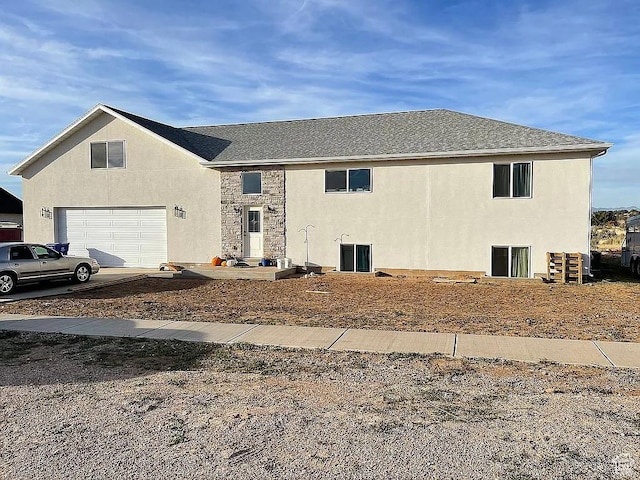 view of front of house with stucco siding, an attached garage, stone siding, and roof with shingles