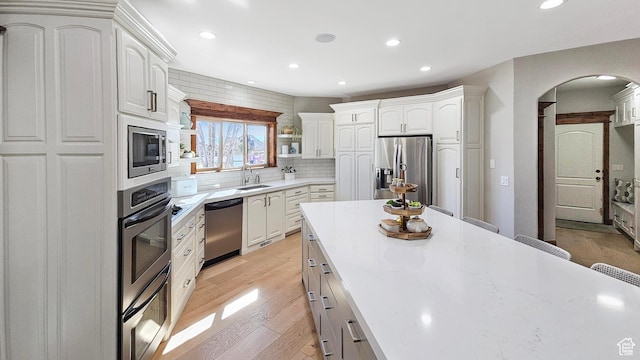 kitchen featuring light wood-style floors, a sink, backsplash, stainless steel appliances, and arched walkways
