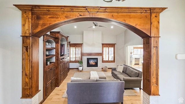 living area with light wood-style flooring, arched walkways, ceiling fan, and a glass covered fireplace