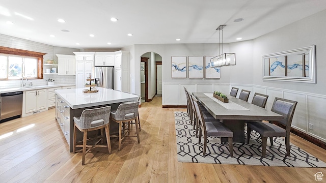 dining room with arched walkways, a wainscoted wall, light wood-style flooring, and an inviting chandelier