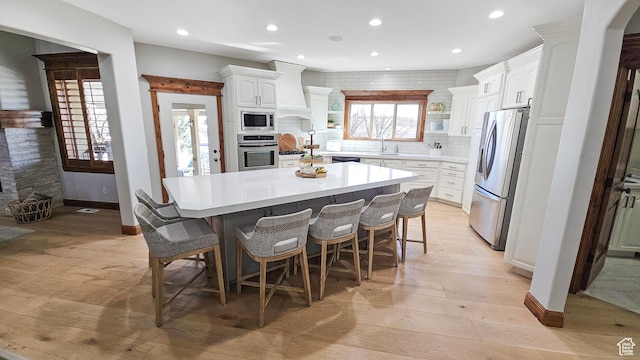 kitchen with appliances with stainless steel finishes, white cabinetry, custom range hood, a breakfast bar area, and backsplash
