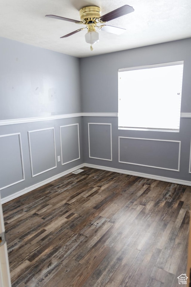 spare room featuring dark wood-style floors, a decorative wall, and ceiling fan