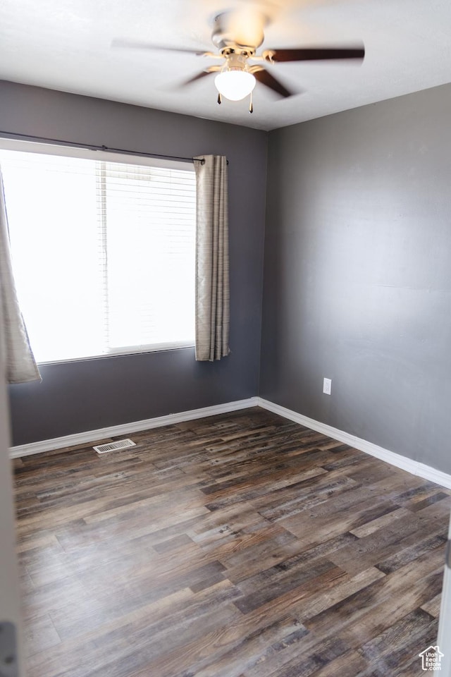 spare room with dark wood-style flooring, visible vents, baseboards, and ceiling fan