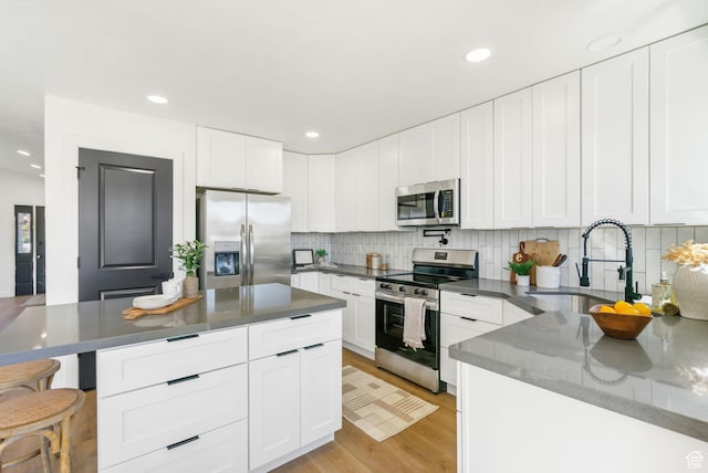 kitchen featuring backsplash, a sink, white cabinetry, light wood-type flooring, and stainless steel appliances