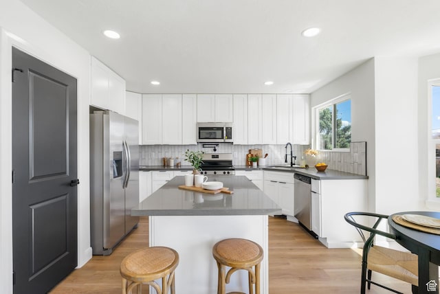 kitchen with a kitchen bar, stainless steel appliances, dark countertops, a sink, and backsplash