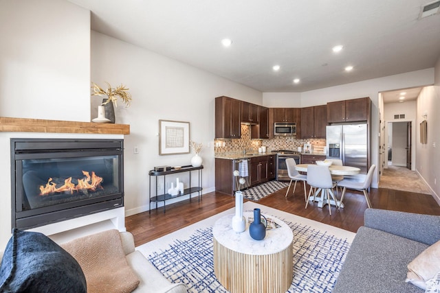 living room featuring dark wood-style flooring, visible vents, baseboards, recessed lighting, and a glass covered fireplace