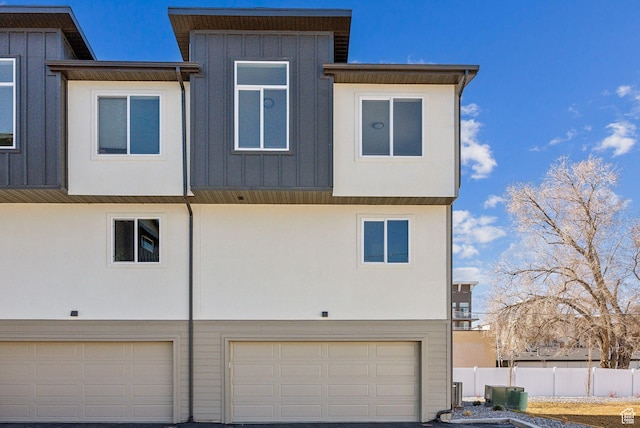 exterior space with driveway, fence, a garage, board and batten siding, and stucco siding