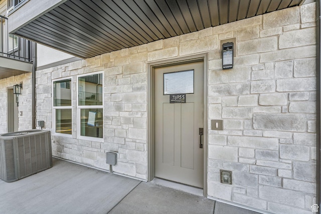 property entrance featuring stone siding and central AC unit