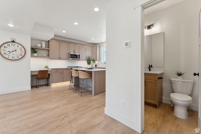 kitchen featuring light wood-style flooring, a kitchen breakfast bar, stainless steel microwave, open shelves, and backsplash