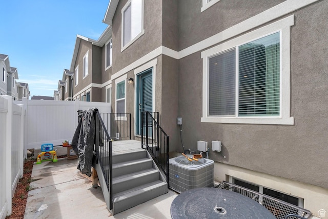 doorway to property featuring a patio area, stucco siding, fence, and central air condition unit