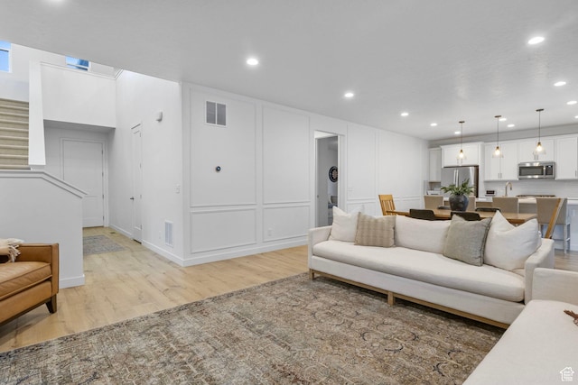living area featuring light wood-style flooring, a decorative wall, visible vents, and recessed lighting