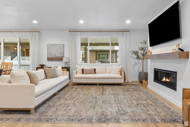 living room with a textured ceiling, a glass covered fireplace, recessed lighting, and wood finished floors