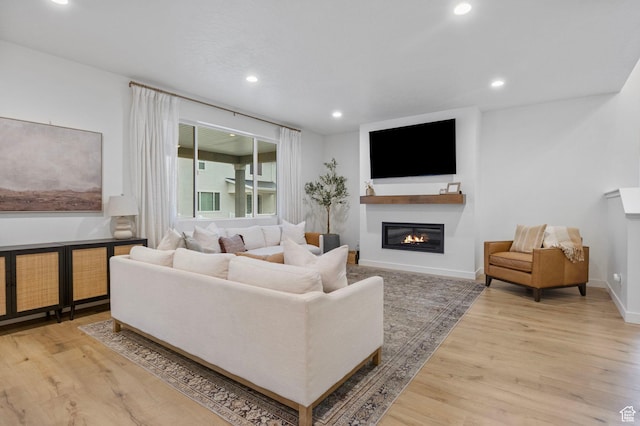 living room featuring baseboards, recessed lighting, wood finished floors, and a glass covered fireplace