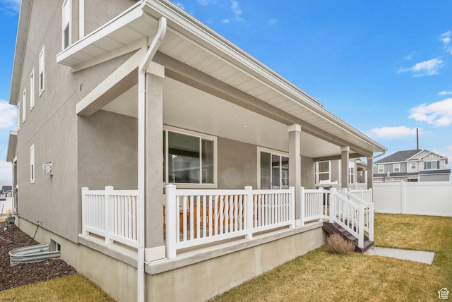 view of home's exterior with covered porch, stucco siding, fence, and a lawn