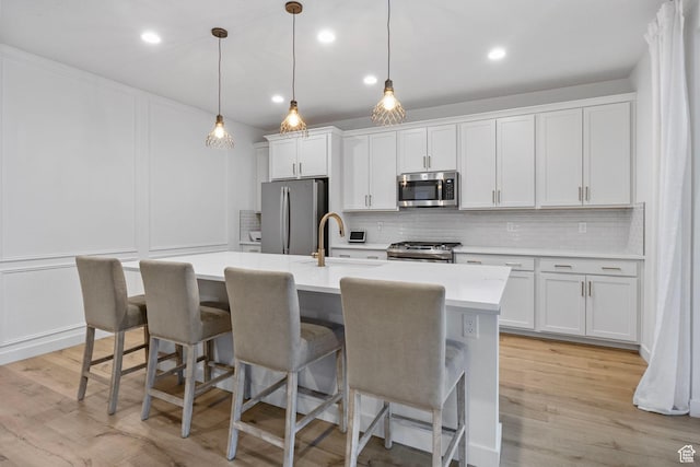 kitchen with a sink, appliances with stainless steel finishes, an island with sink, and decorative backsplash