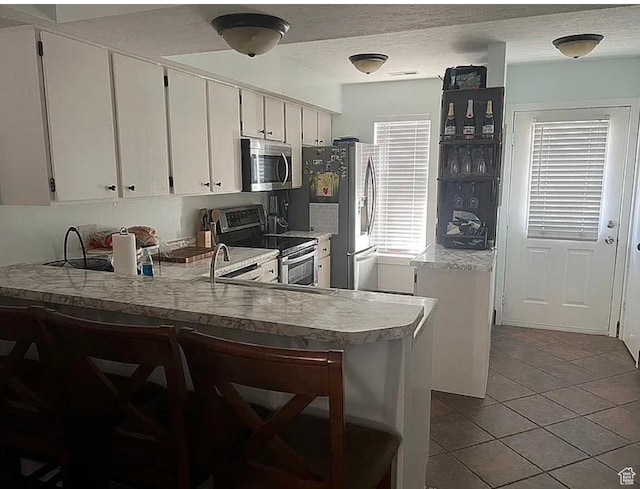 1418 W Telegraph Hill Dr, Taylorsville, UT 84123 - kitchen featuring light countertops, white cabinets, a peninsula, tile patterned floors, and appliances with stainless steel finishes