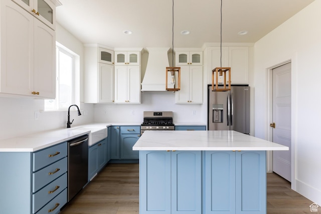 kitchen featuring a sink, a kitchen island, appliances with stainless steel finishes, custom range hood, and blue cabinetry