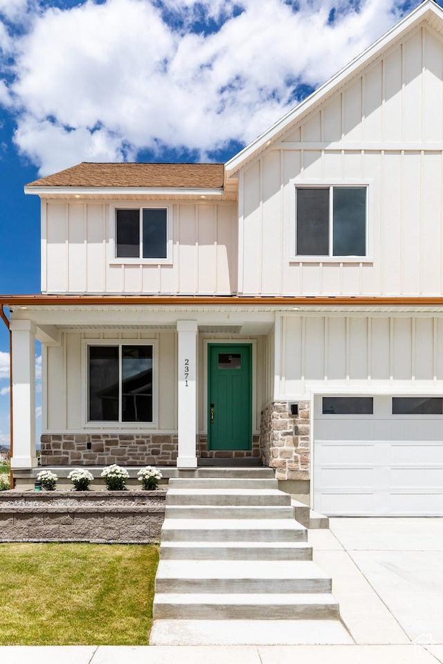 modern farmhouse with stone siding, an attached garage, board and batten siding, a shingled roof, and a porch