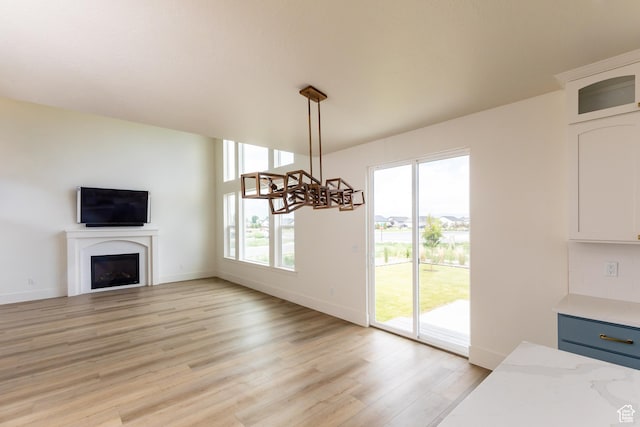 unfurnished living room with baseboards, a fireplace, an inviting chandelier, and light wood-type flooring