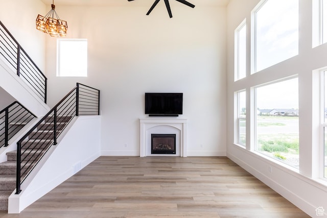 unfurnished living room with a high ceiling, light wood-style flooring, baseboards, and stairway