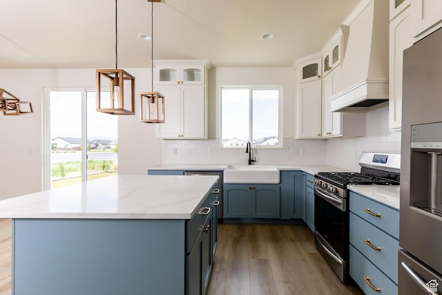 kitchen featuring a sink, a center island, stainless steel appliances, custom range hood, and white cabinets