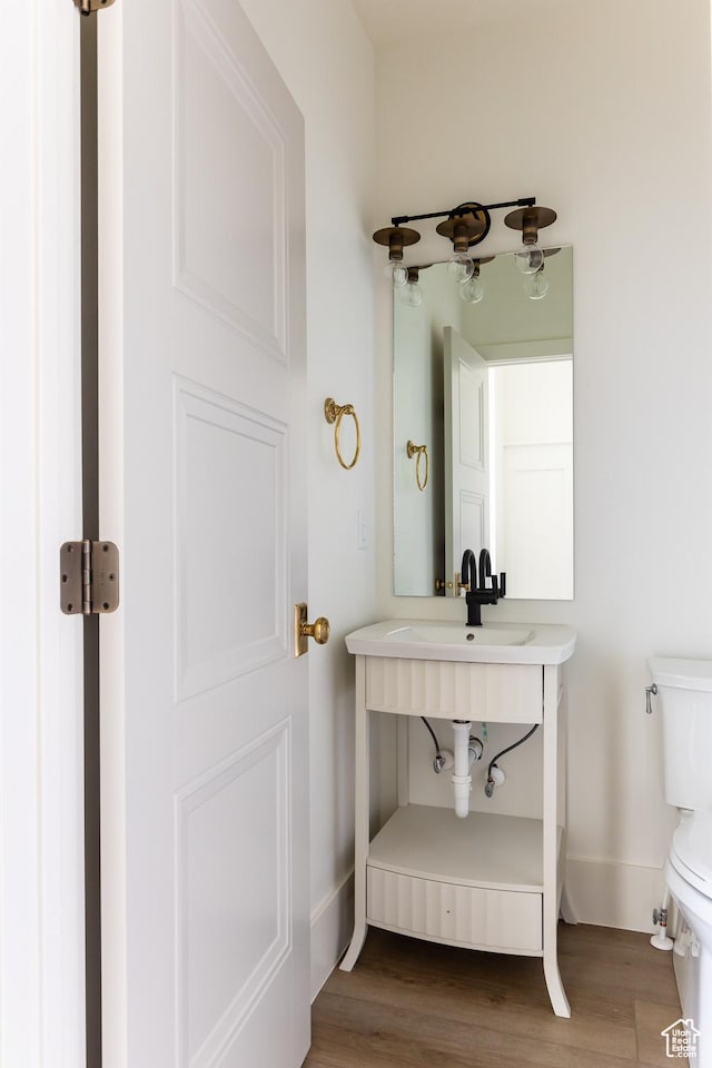 bathroom with toilet, a sink, baseboards, and wood finished floors