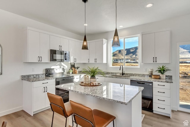 kitchen with a sink, a breakfast bar area, black appliances, and light wood-type flooring