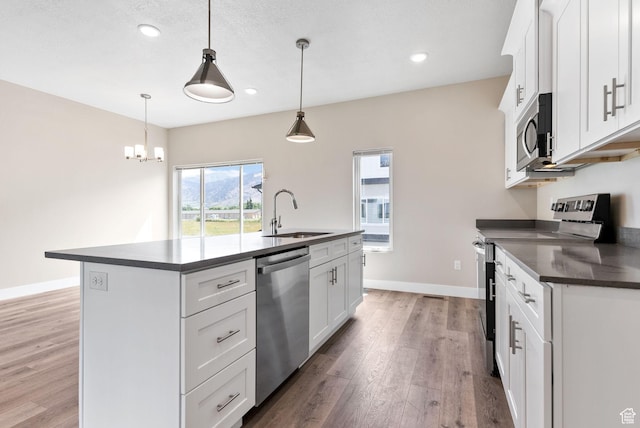 633 E 730 N, Hyrum, UT 84319 - kitchen with stainless steel appliances, dark countertops, a center island with sink, a sink, and light wood-style floors