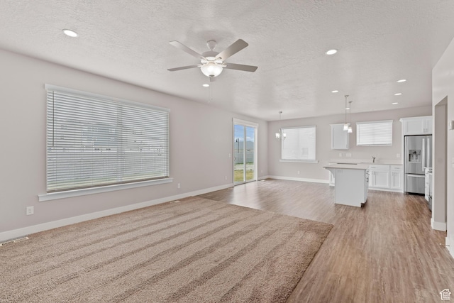 unfurnished living room with plenty of natural light, ceiling fan, light wood-style floors, and visible vents