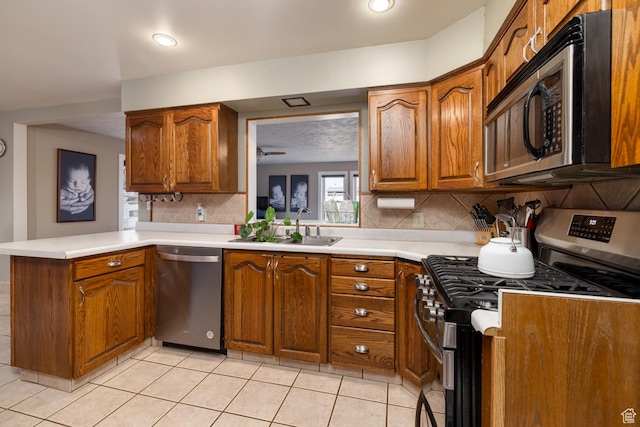 kitchen with decorative backsplash, brown cabinets, a sink, a peninsula, and stainless steel appliances