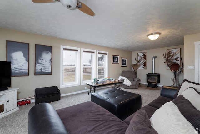 living area featuring baseboards, a wood stove, ceiling fan, and carpet floors