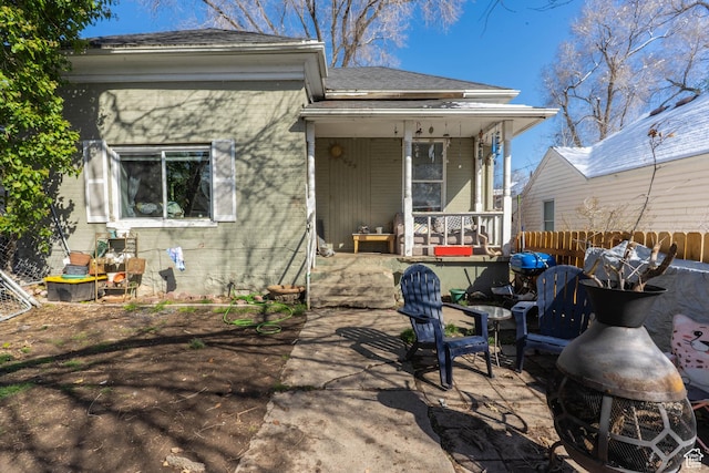 back of house with a porch, a shingled roof, fence, and a patio